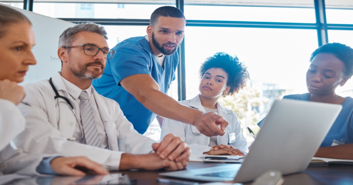 Doctor, nurse, and healthcare accounting team meeting to discuss financial management and modern ERP, all looking at a computer on the table